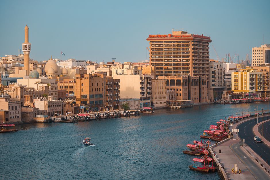 A beautiful view of Dubai Creek showcasing traditional buildings and abra boats in warm daylight
