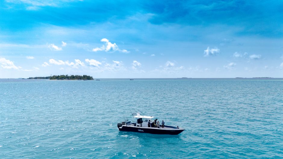 A boat with people cruising in the vibrant blue waters near a tropical island in the Maldives