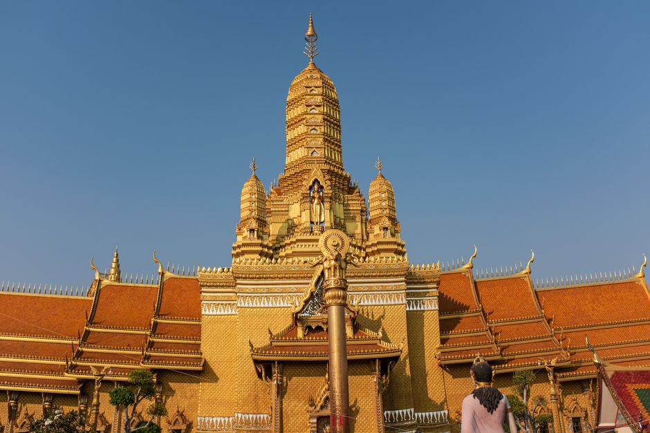 A magnificent golden Buddhist temple in Bangkok against a clear sky, showcasing intricate architecture