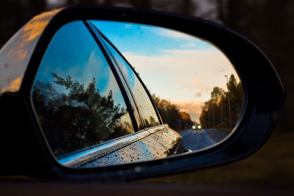 A wet side mirror capturing a dynamic reflection of a road and trees at twilight