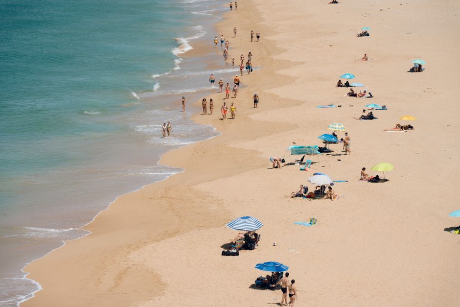 Aerial view of a crowded sandy beach with sunbathers and colorful umbrellas on a sunny day