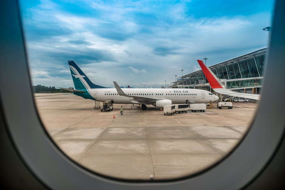 View of airplanes on a tarmac from an airplane window under a blue sky.