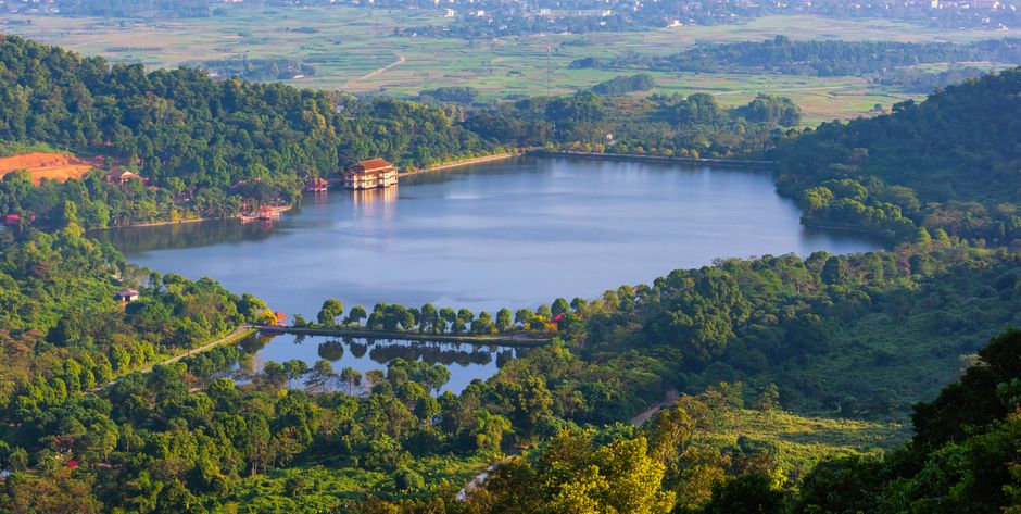 Aerial view of a tranquil lake surrounded by rich greenery and distant fields.