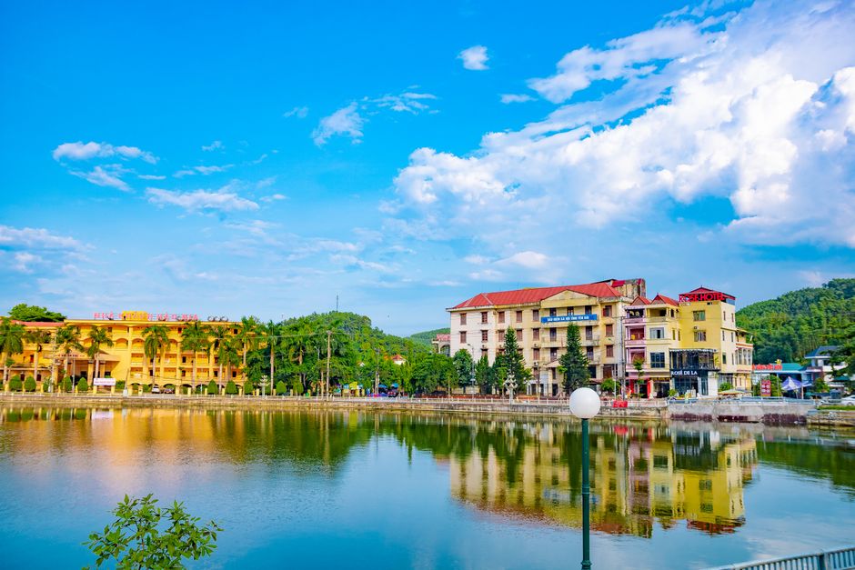 Colorful buildings reflected in a tranquil lake under a clear blue sky in Vietnam.