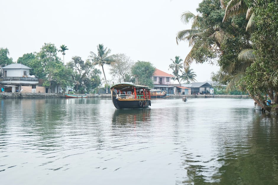Serene view of a houseboat on Kerala's lush, tranquil backwaters with coconut trees and quaint houses.