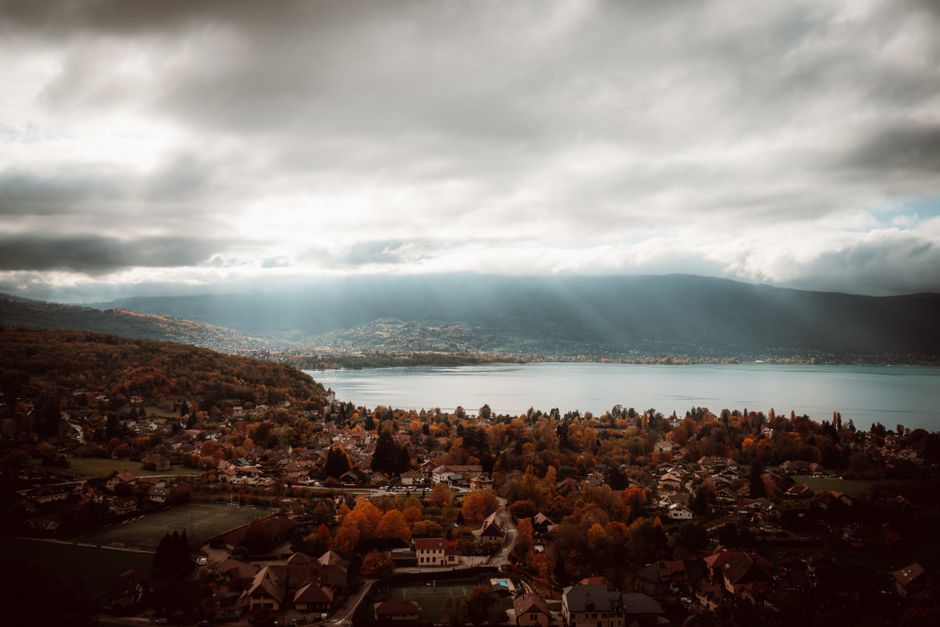 Breathtaking aerial view of Lake Annecy with autumn foliage and dramatic clouds