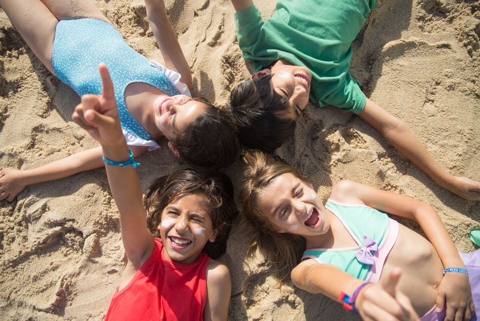 Happy group of diverse children lying on a sunlit beach, enjoying summer fun.