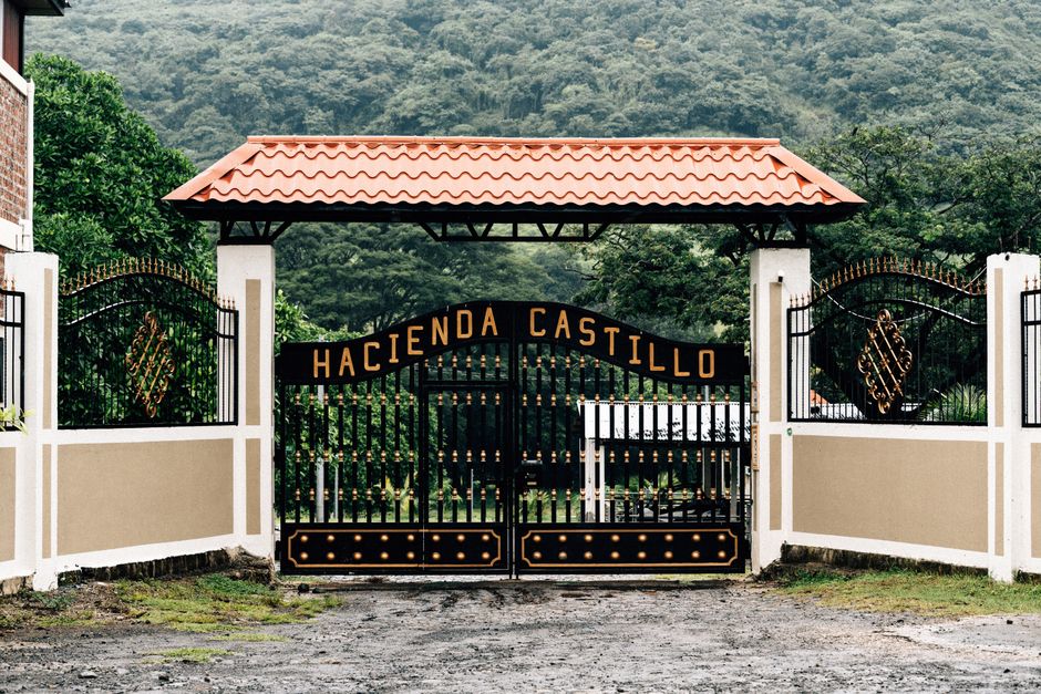 Photograph of the entrance gate to Hacienda Castillo, surrounded by lush greenery and mountains.