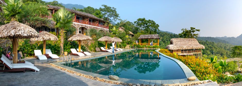 Calm swimming pool with blue water with deckchairs and umbrellas near small hotel in south eastern style in tropical terrain