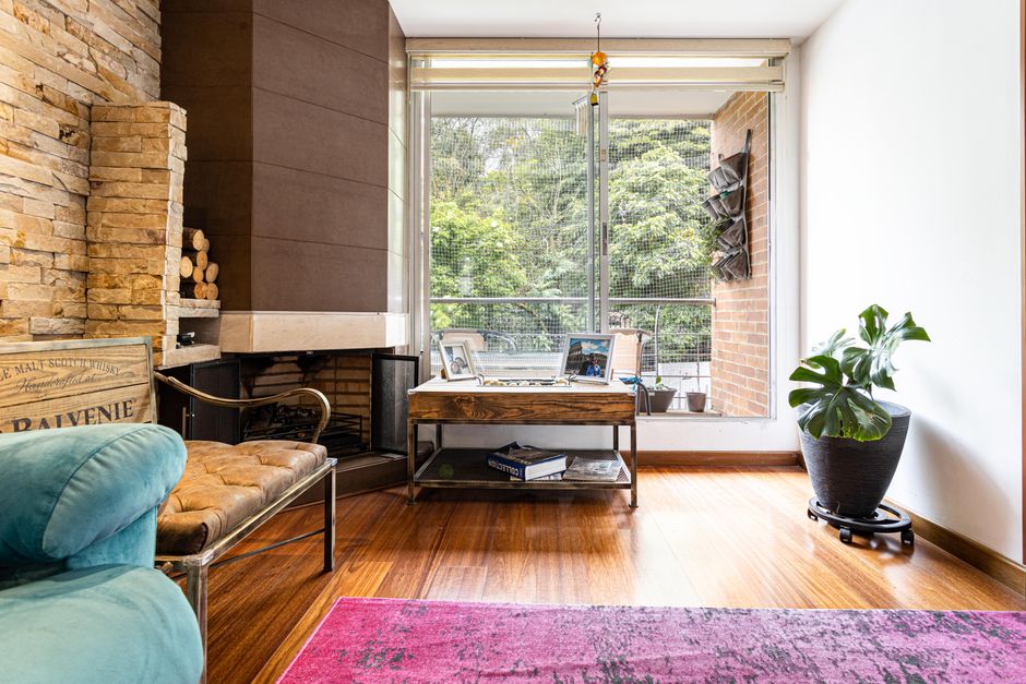 Cozy living room in Bogotá featuring a fireplace, modern decor, and lush greenery view.