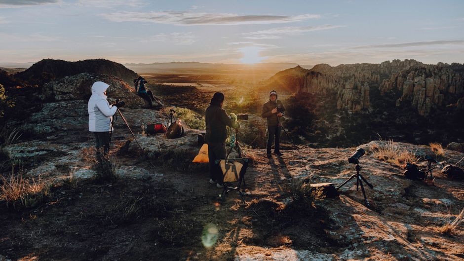 Group of photographers with tripods capturing a stunning sunrise on a rocky cliff. Perfect for adventure and travel themes.