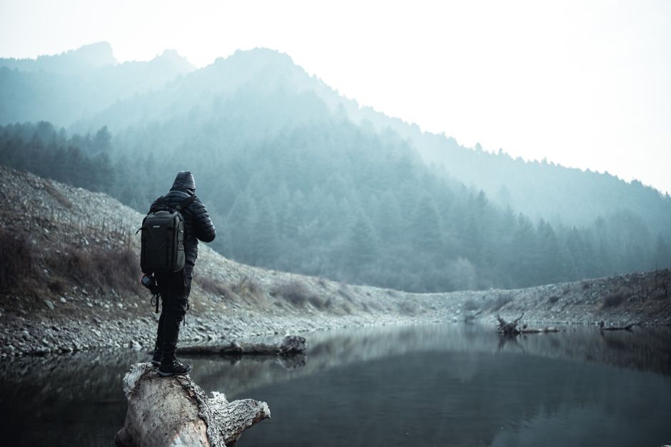 A lone hiker in a jacket explores a foggy mountain landscape by a tranquil lake.