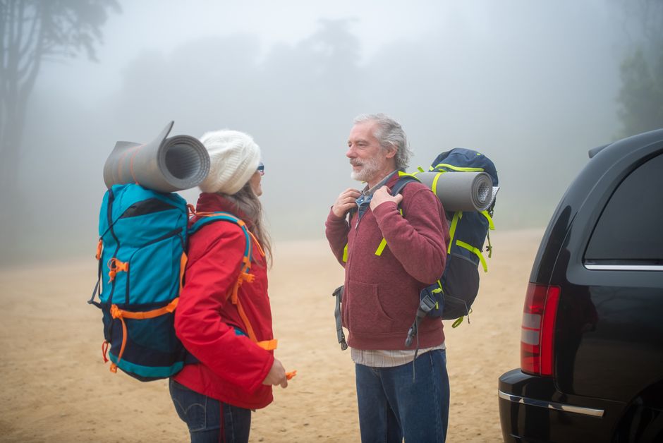 Elderly couple with backpacks getting ready for a hike in foggy Portugal outdoors.