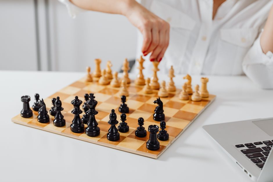 A person strategically playing chess on a wooden board in a bright office setting.