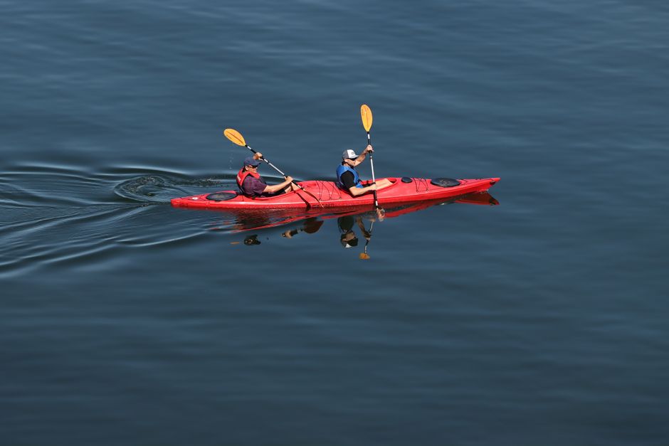 Two people kayaking in a red kayak on a serene lake in Sweden. Outdoor recreation and adventure.