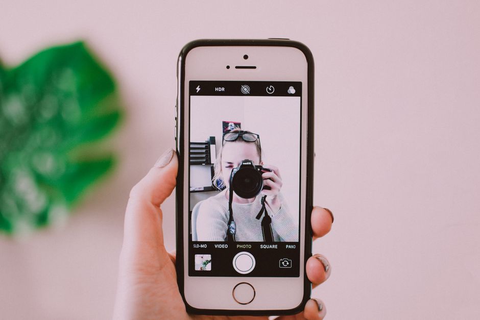 A person taking a selfie with a camera through a smartphone, showing a creative reflection.