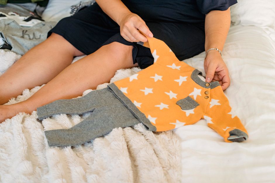 Crop anonymous female in dress resting on soft bed while demonstrating new wear for infant child