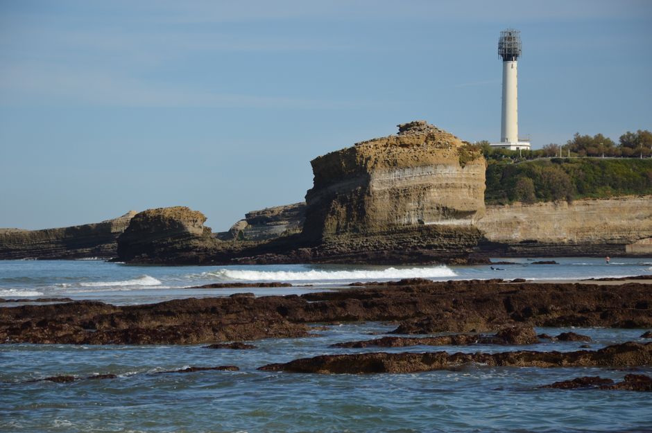 Lighthouse towering over stunning rock formations and crashing waves on a sunny day
