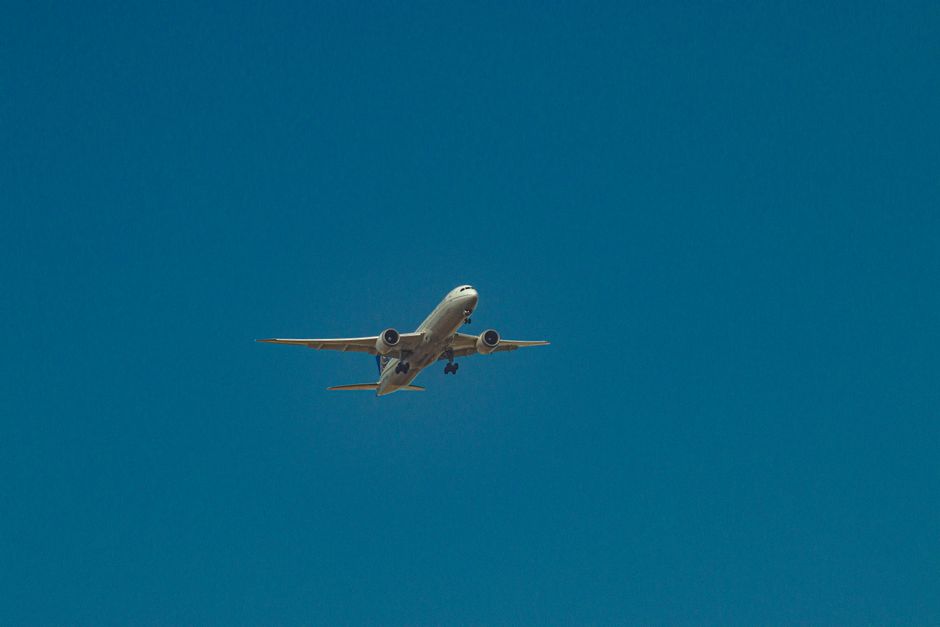 From below of airplane with turbines and landing gear flying over clear blue sky