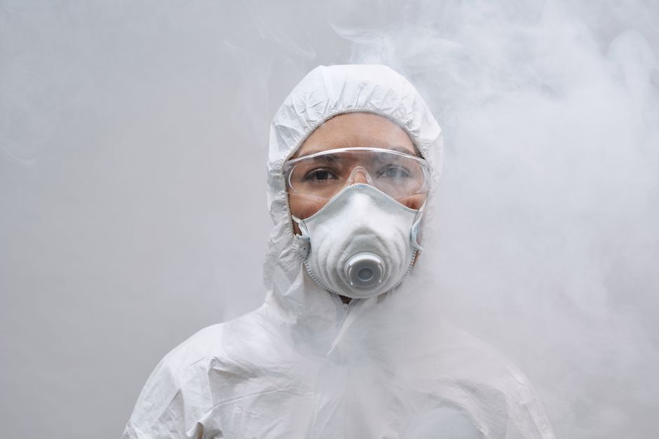 Close-up of person wearing protective suit, mask, and goggles amidst smoke.