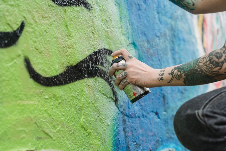 Dynamic close-up of a tattooed artist spray painting an urban graffiti mural in vivid colors.