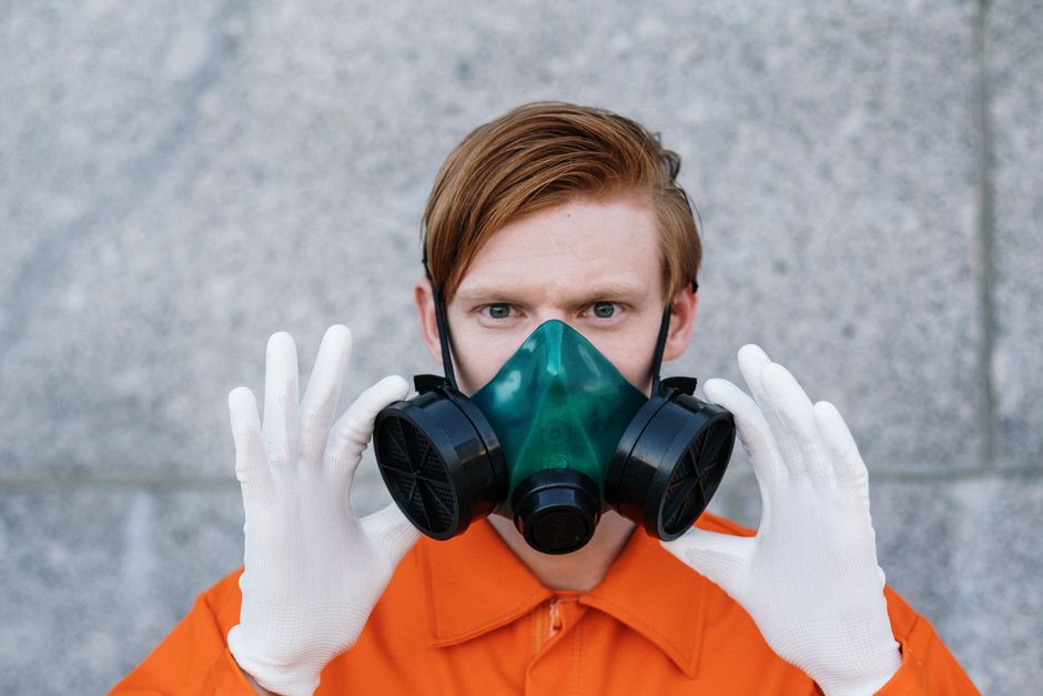 A young adult wearing a respirator mask and gloves for safety against toxins or pollutants.