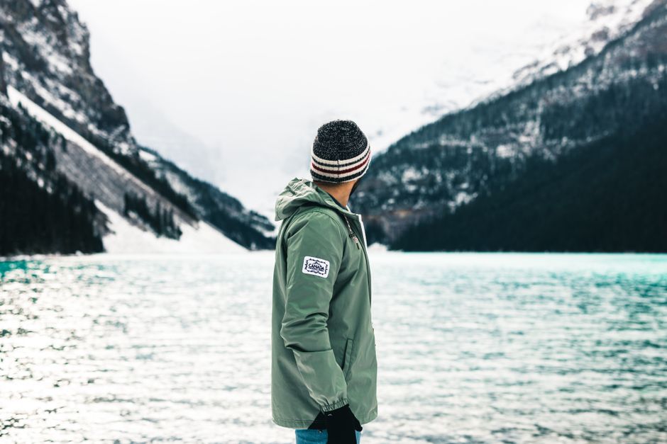 Man in winter jacket standing by Lake Louise, Alberta, surrounded by snow-capped mountains