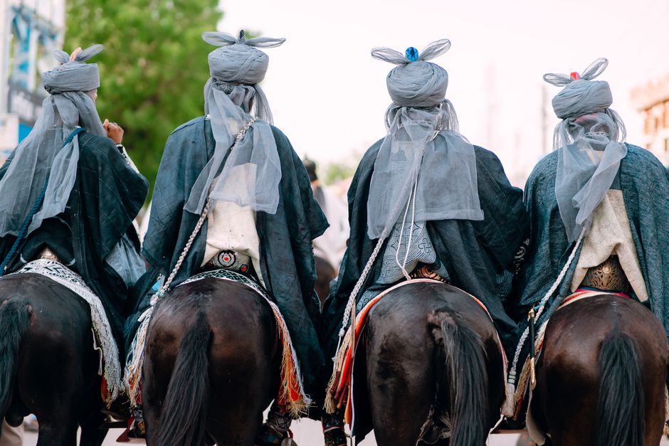 Four riders in traditional attire on horseback in a cultural parade, showcasing rich tradition and heritage.