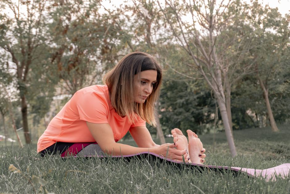 A woman performs a stretching exercise in a park on a sunny day, promoting outdoor fitness and wellness.