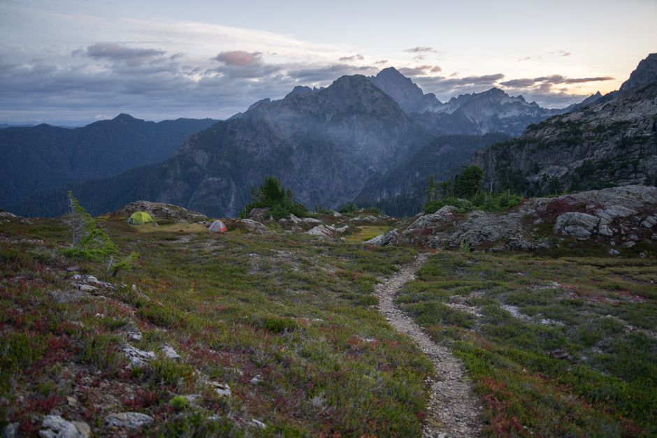 Peaceful morning view of a campsite in the Washington mountains with rocky trails and distant peaks.