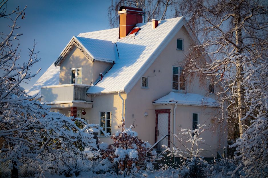 Scenic winter view of a charming house with snow-covered roof, surrounded by frosted trees.