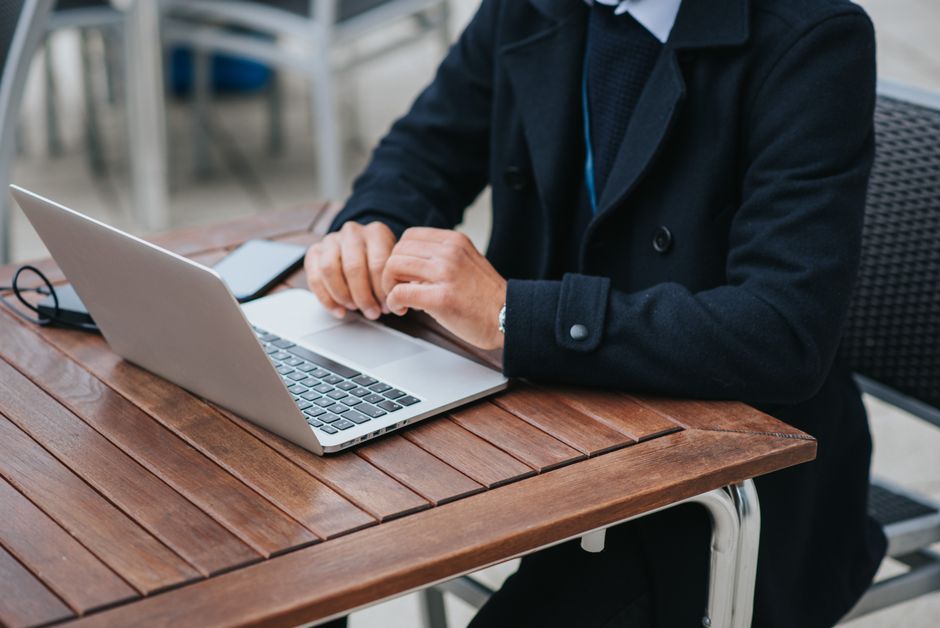 Crop anonymous male entrepreneur in formal apparel sitting at cafeteria table with netbook and smartphone in daytime