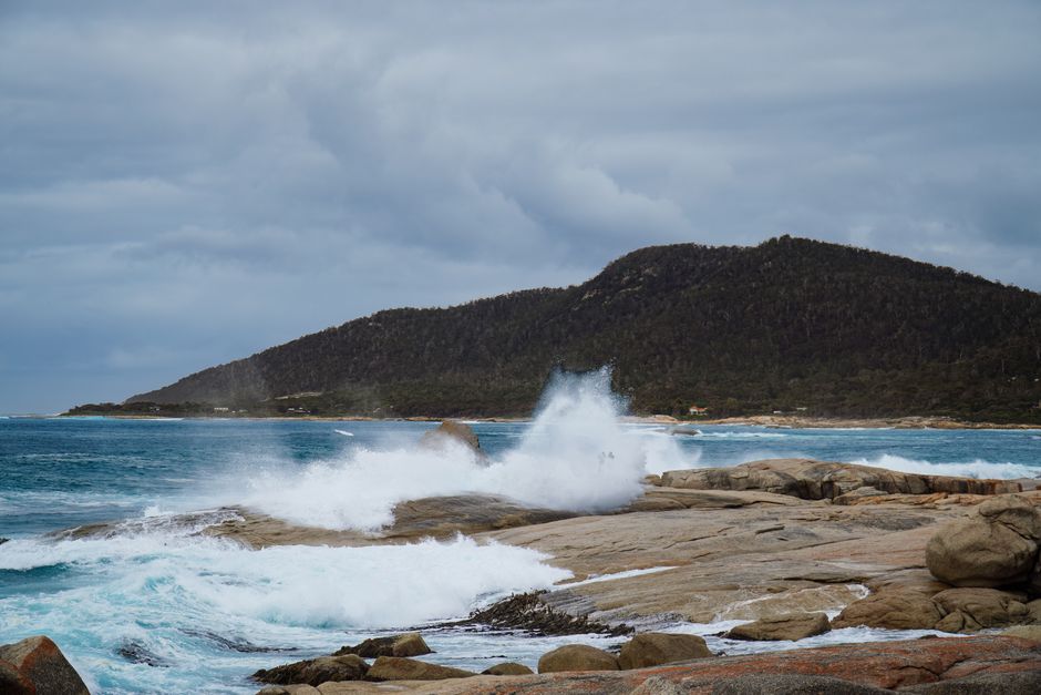 Powerful waves crashing against rugged rocks on a cloudy day in Bicheno, Tasmania