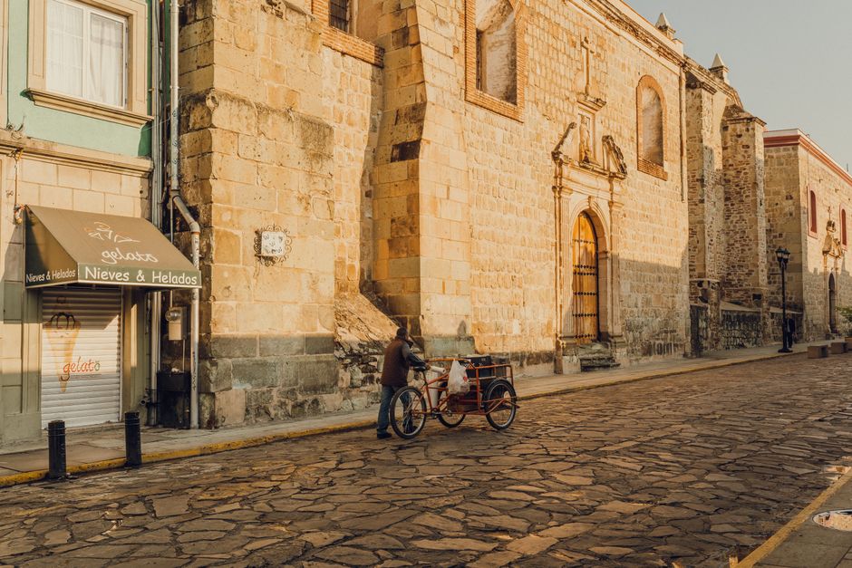Quiet street in Oaxaca, México featuring historic stone buildings and a local man with a bicycle cart