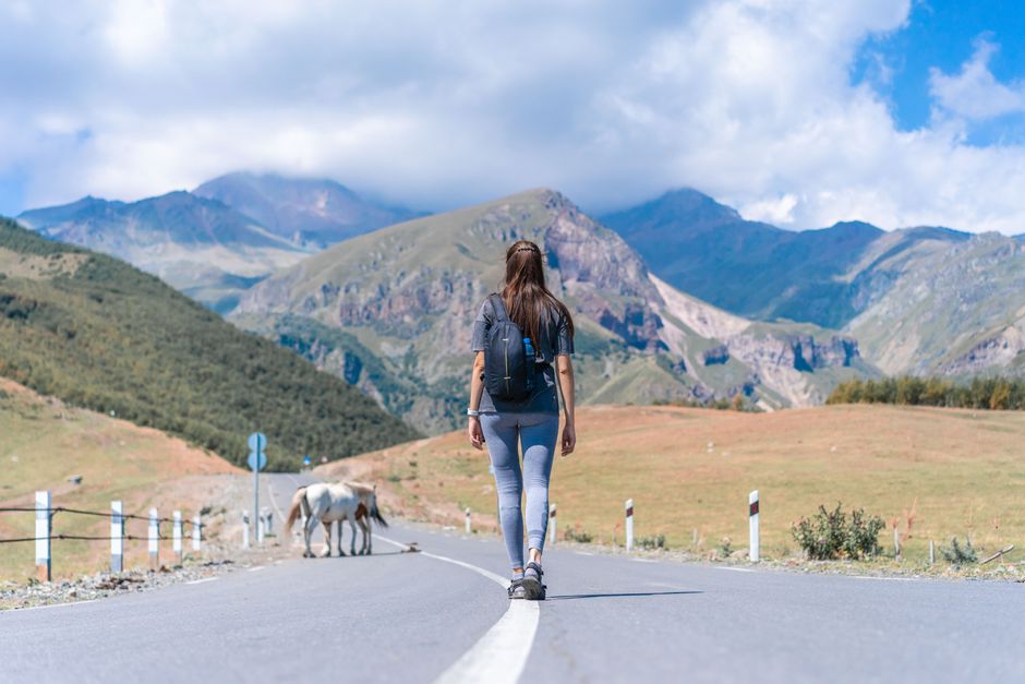 Back view of woman with backpack walking on road in Stepantsminda, Georgia's stunning mountains.