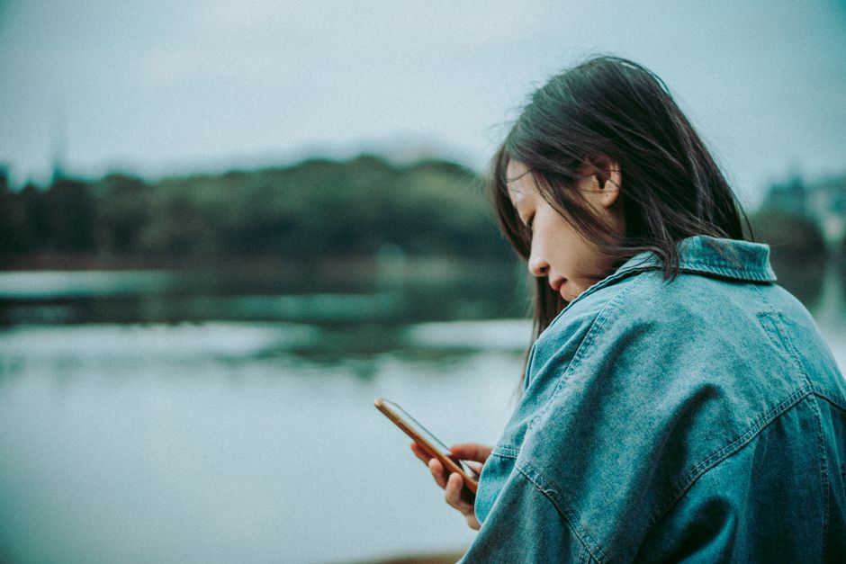 A woman enjoys a serene moment by the lake, engrossed in her smartphone.