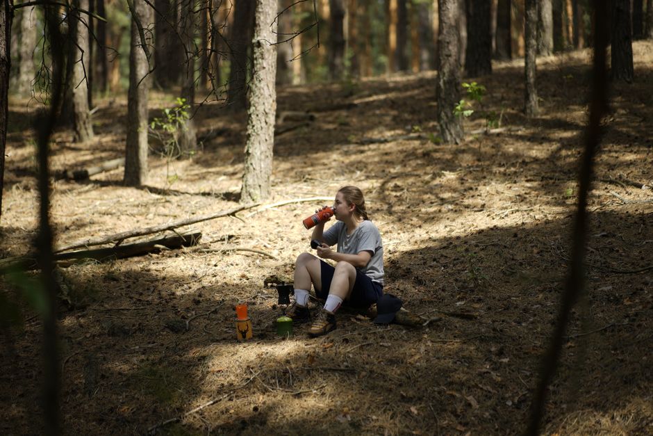 A woman relaxes in a sunny forest, enjoying a drink and solitude.