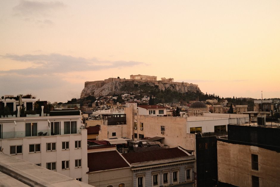 Scenic sunset view of the Acropolis in Athens, Greece, framed by city rooftops and a pastel sky