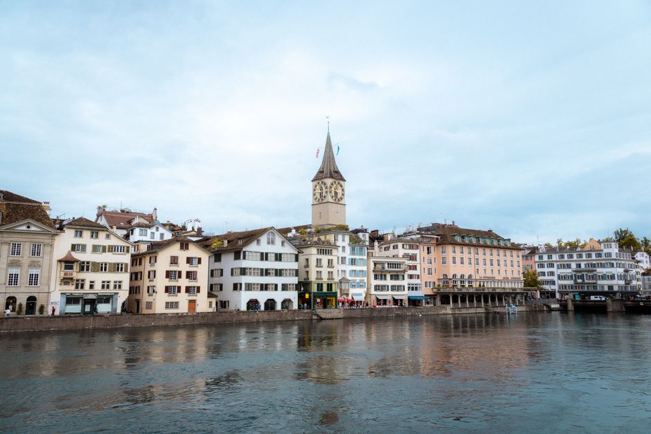 Scenic view of Zürich's historic buildings and clock tower by Lake Zürich under a cloudy sky