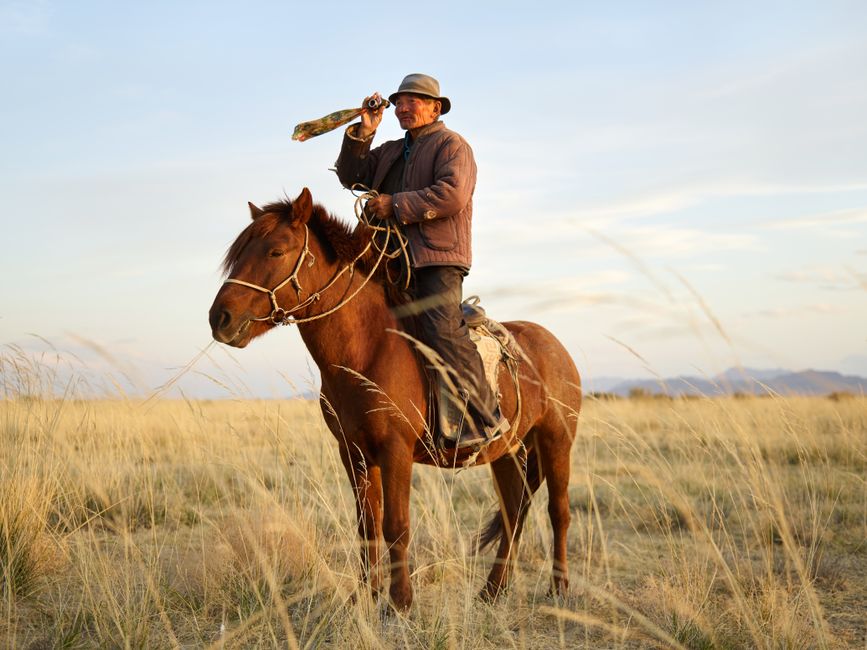 Senior Asian horseman wearing national cloth looking away through vintage monocular standing up in stirrups wh