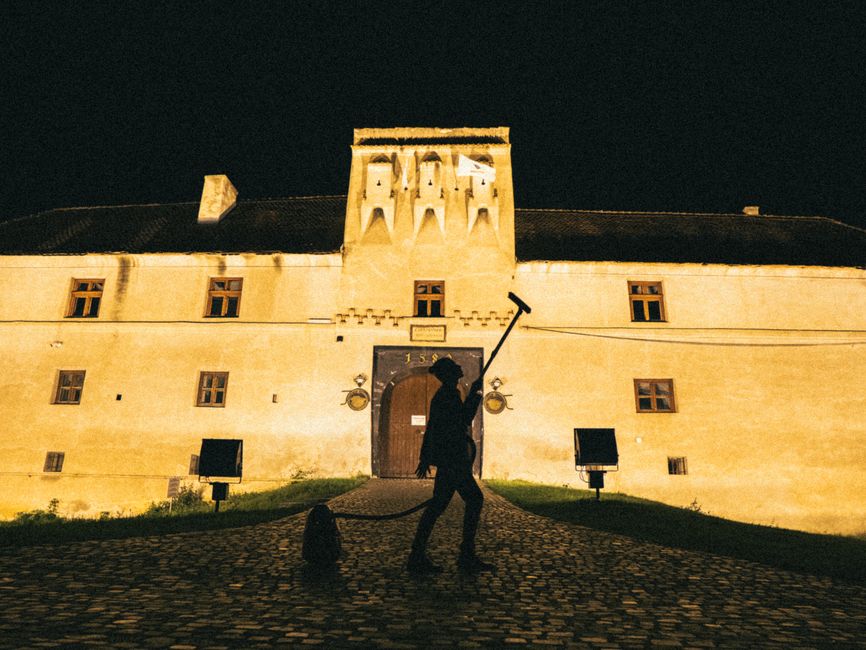 Silhouetted figure holding tool against illuminated historic fortress at night