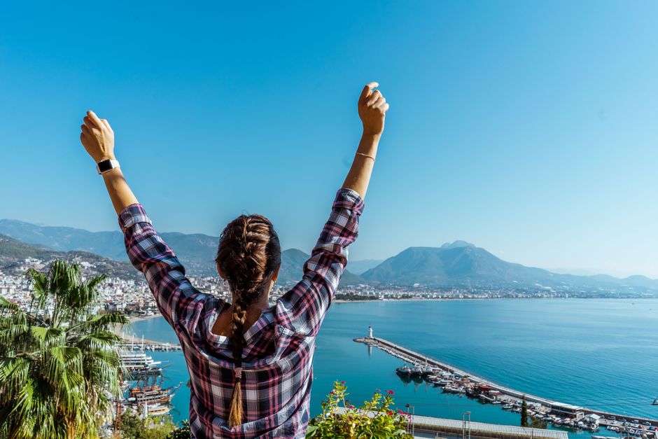 Woman with raised arms enjoying Alanya harbor view in Turkey on a sunny day.