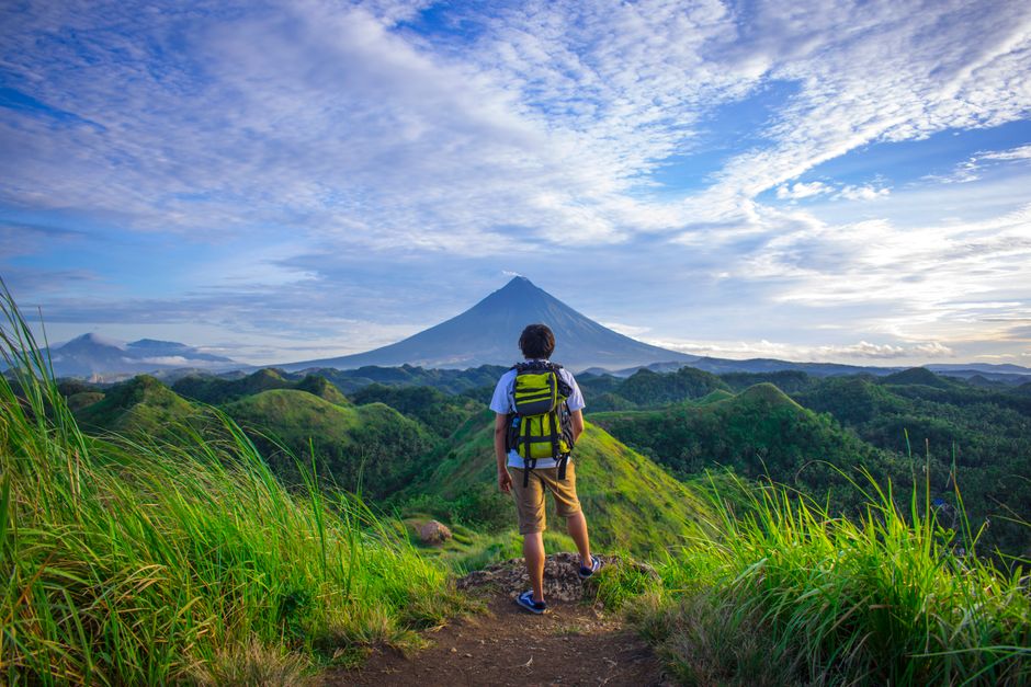 A hiker enjoys the scenic view of Mount Mayon in the lush Bicol countryside.
