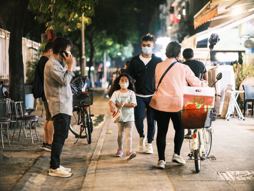 Urban street at night with people wearing face masks, depicting a scene of the new normal.