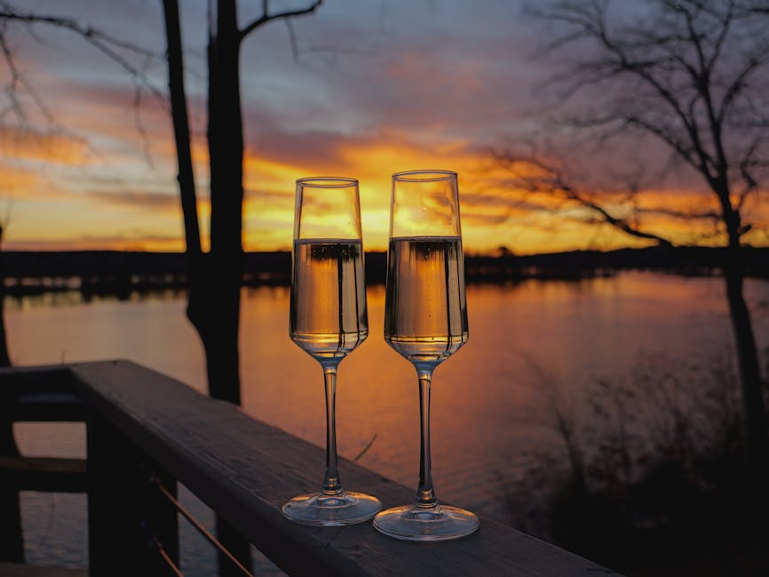 Two champagne glasses at sunset on a balcony overlooking a serene lake.