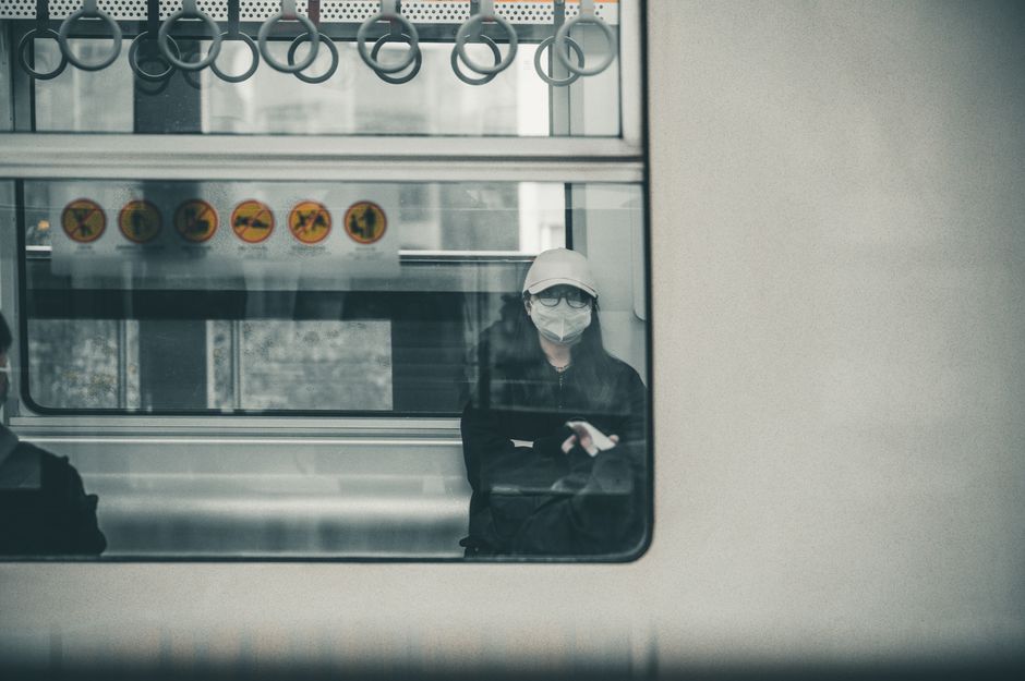 A lone commuter wearing a mask sits inside a train, reflecting modern travel norms.