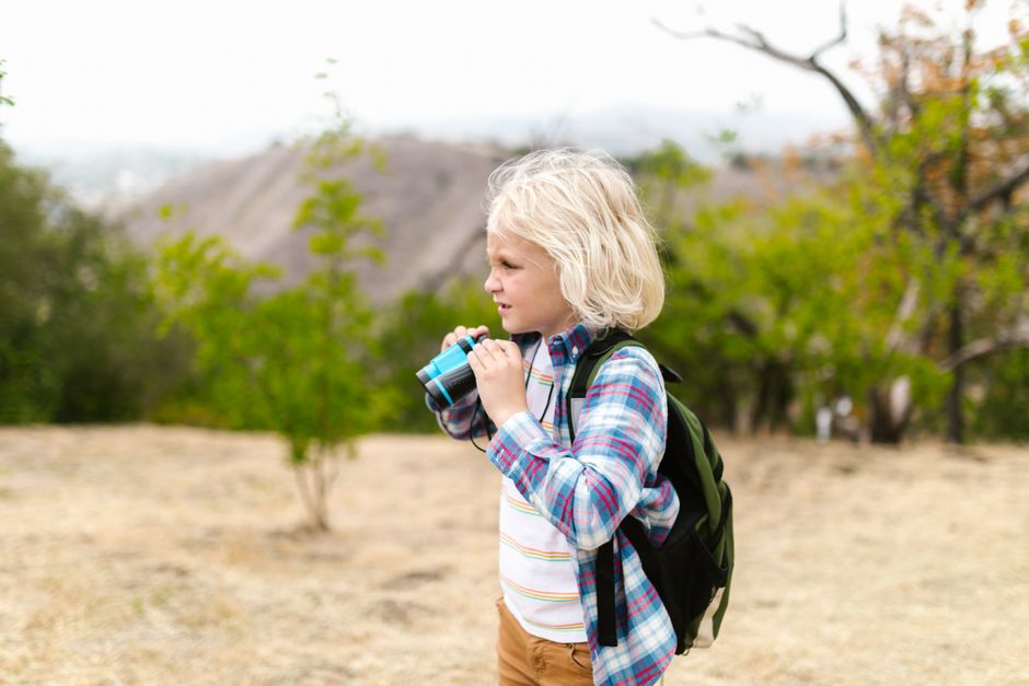 A cheerful child holding binoculars outdoors, enjoying a nature adventure.