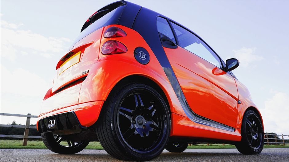 Bright orange Smart car parked on asphalt in Knebworth, England, showcasing sleek design.