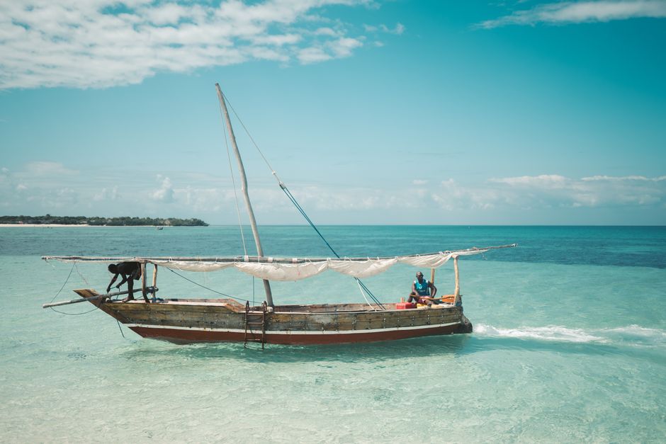 Two local fishermen navigate a traditional dhow on the clear waters of Zanzibar under a bright blue sky