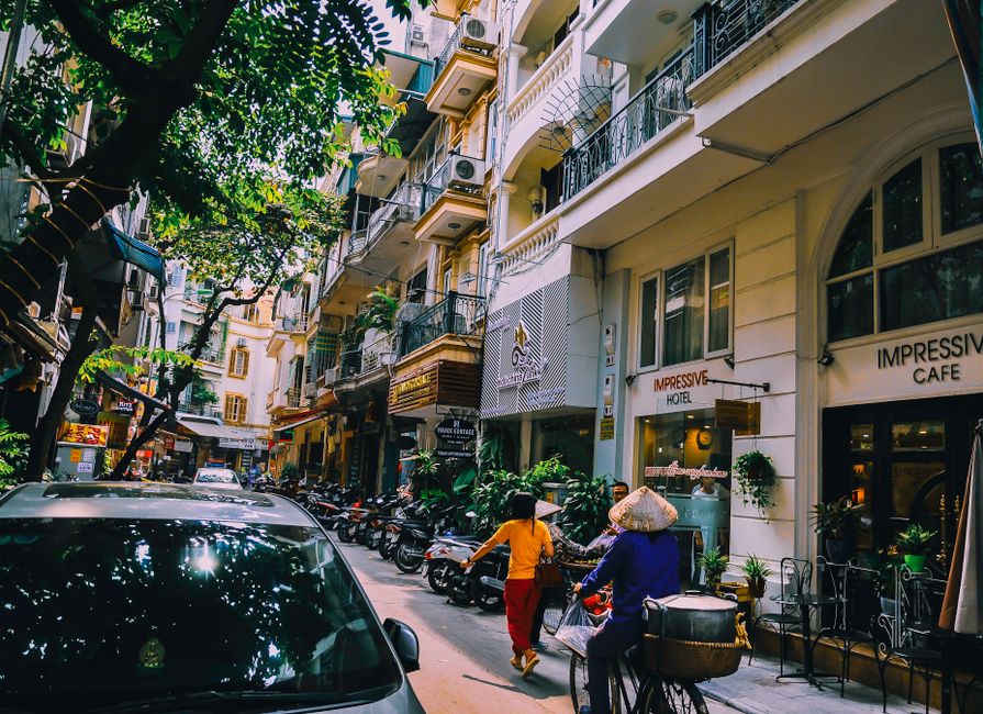 Vibrant street life in Hanoi with locals, cafes, and motorbikes on a sunny day